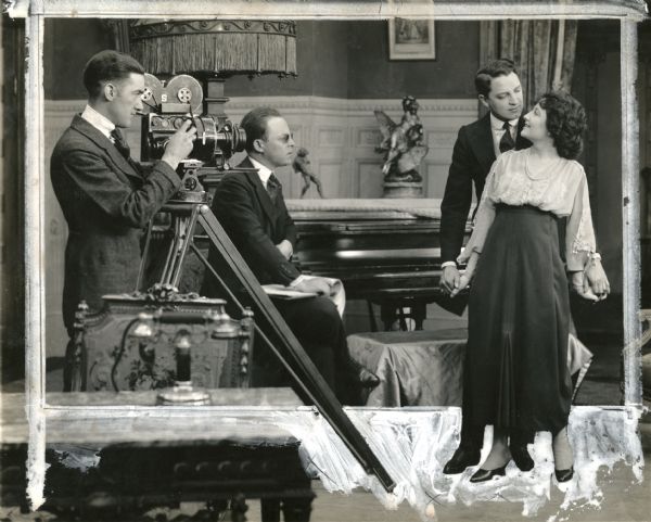 Essanay silent film director Harry Beaumont, wearing tinted pince-nez, watches Bryant Washburn and Hazel Daly act out a scene for "Filling His Own Shoes." The cameraman Will E. Smith cranks a Bell & Howell model 2709 motion picture camera.